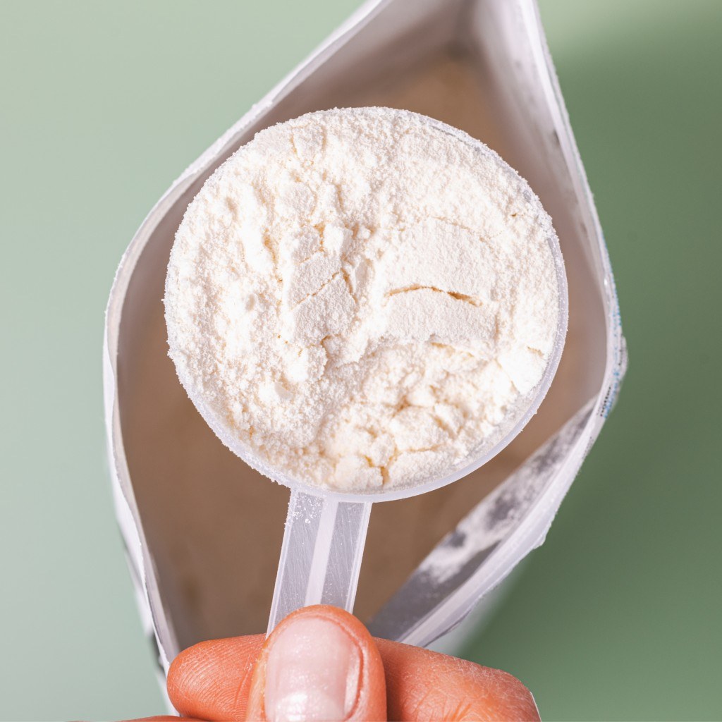 Scoop of pale hemp protein powder lifted from a pouch